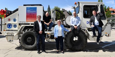 Präsentation Messkampagne GIGA-M Foto: Ein Vibro-Truck, davor stehen vier Männer vor bzw. auf dem Truck, in ihrer Mitte eine Frau. Alle schauen in die Kamera.