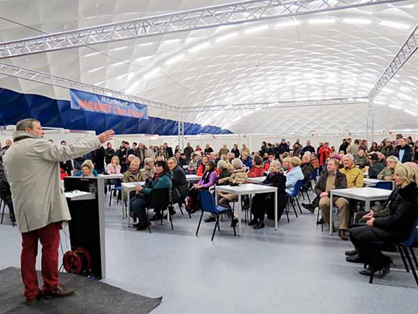 Foto: Ernst Weidenbusch, Stellvertreter des Landrats, spricht zu den zahlreichen Besuchern, die in die Traglufthalle gekommen sind. Sie sitzen auf den Stühlen im Aufenthaltsbereich oder stehen an den Seiten des Aufenthaltsbereiches.