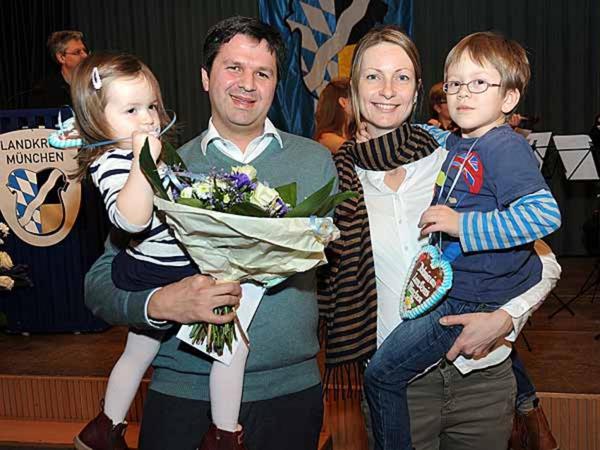 Foto: Frederico Ayrosa Nascimento und seine Frau Daniela tragen die beiden gemeinsamen Kinder auf dem Arm. Herr Nascimento hält zudem den Blumenstrauß, den er für den Vortrag seines Erfahrungsberichts erhalten hat, in der Hand.